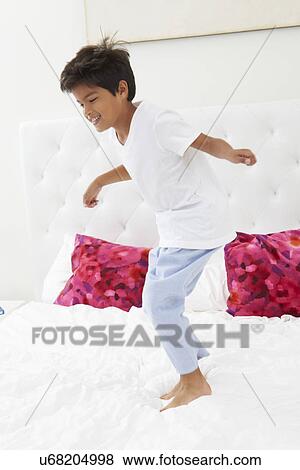 Stock Photo - Boy Jumping On Bed Wearing Pajamas. Fotosearch