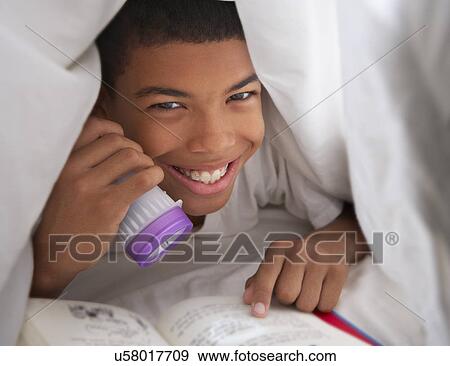 Stock Photo - Boy Reading Book With Torch Under Duvet. Fotosearch