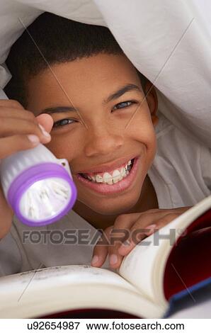 Stock Photo - Boy Reading Book With Torch Under Duvet. Fotosearch