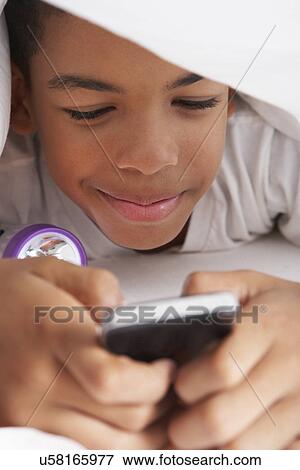 Stock Photo - Boy Using Mobile Phone Under Duvet. Fotosearch