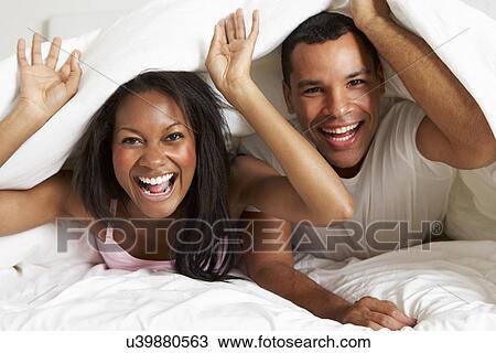 Stock Image - Couple Relaxing In Bed Hiding Under Duvet. Fotosearch