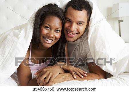 Stock Photograph - Couple Relaxing In Bed Hiding Under Duvet. Fotosearch
