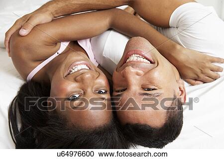 Stock Image - Couple Relaxing In Bed Wearing Pajamas. Fotosearch
