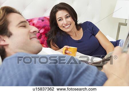 Stock Image - Couple Relaxing In Bed With Coffee And Newspaper. Fotosearch