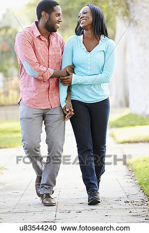 Stock Image - Couple Walking Along Suburban Street Together. Fotosearch