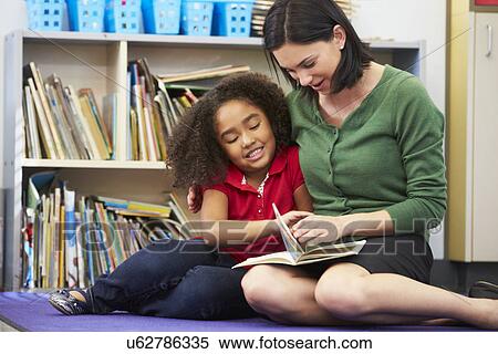 Stock Photography - Elementary Pupil Reading With Teacher In Classroom. Fotosearch