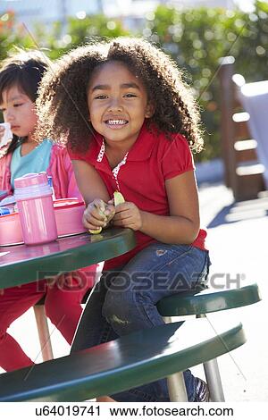 Stock Image - Elementary Pupil Sitting At Table Eating Lunch. Fotosearch