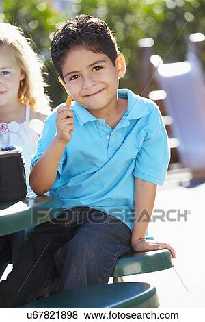 Stock Photo - Elementary Pupil Sitting At Table Eating Lunch. Fotosearch