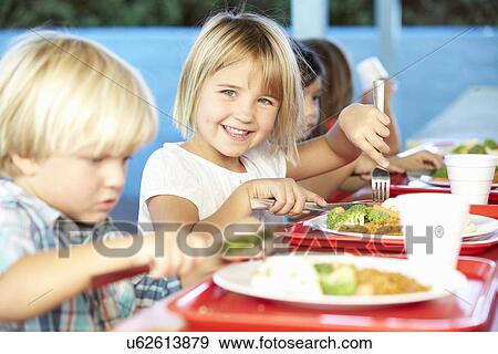 Stock Photo - Elementary Pupils Enjoying Healthy Lunch In Cafeteria. Fotosearch