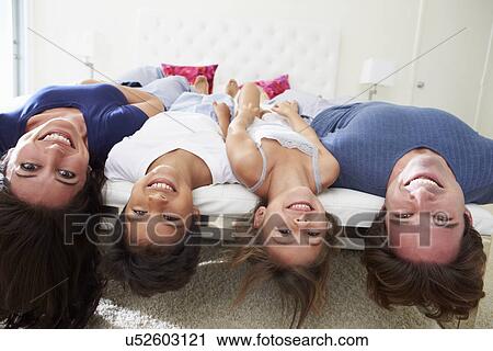 Stock Image - Family Lying Upside Down On Bed In Pajamas Together. Fotosearch
