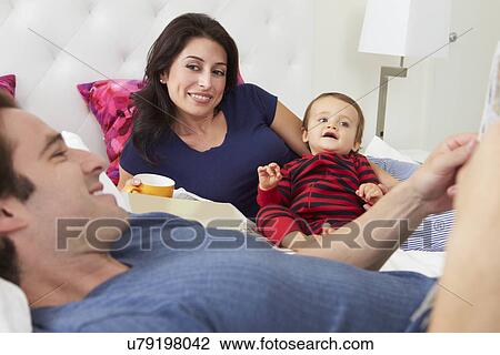 Stock Image - Family Relaxing In Bed With Coffee And Newspaper. Fotosearch
