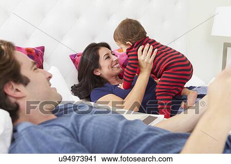 Stock Image - Family Relaxing In Bed With Young Son. Fotosearch