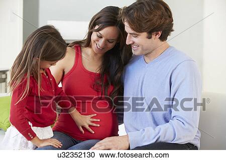 Stock Image - Family With Pregnant Mother Relaxing On Sofa Together. Fotosearch