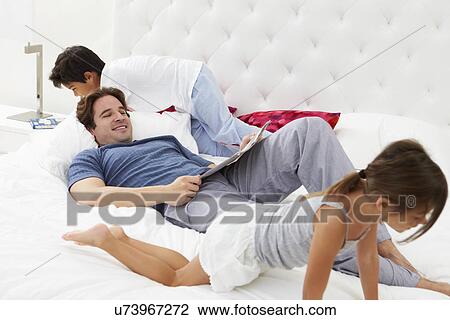 Stock Image - Father And Children Relaxing In Bed Together. Fotosearch