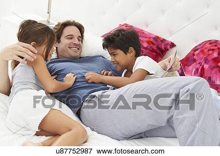 Father And Children Relaxing In Bed Together View Large Photo Image Stock Photo - Father And Children Relaxing In Bed Together. Fotosearch