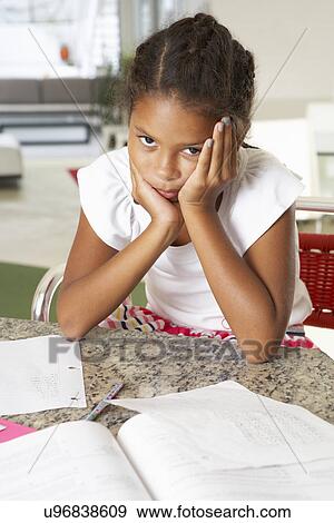Stock Photo - Fed Up Girl Doing Homework In Kitchen. Fotosearch