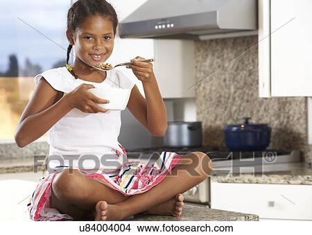 Picture - Girl In Kitchen Eating Bowl Of Breakfast Cereal. Fotosearch