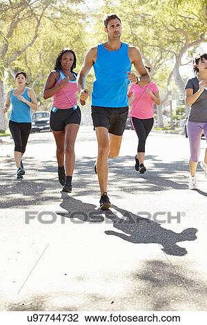 Stock Image - Group Of Women Running Along Street With Personal Trainer. Fotosearch