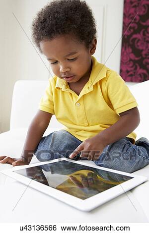Stock Photograph - Happy Boy On Sofa Playing With Digital Tablet. Fotosearch