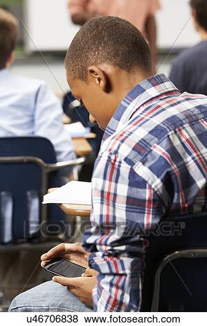 Stock Photo - Male Pupil Sending Text Message In Classroom. Fotosearch