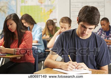 Stock Photo - Male Pupil Studying At Desk In Classroom. Fotosearch