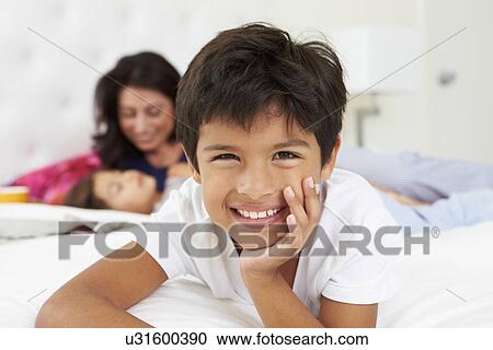 Stock Image - Mother And Children Relaxing In Bed Wearing Pajamas. Fotosearch