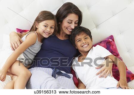 Stock Image - Mother And Children Relaxing In Bed Wearing Pajamas. Fotosearch