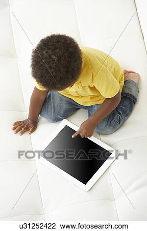 Stock Image - Overhead View Of Boy On Sofa Playing With Digital Tablet. Fotosearch