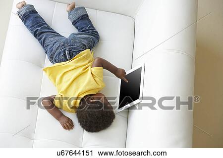Stock Image - Overhead View Of Boy On Sofa Playing With Digital Tablet. Fotosearch