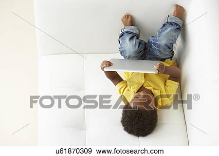 Stock Photo - Overhead View Of Boy On Sofa Playing With Digital Tablet. Fotosearch