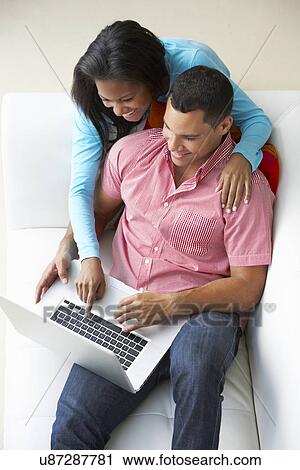 Stock Image - Overhead View Of Couple Relaxing On Sofa Using Laptop. Fotosearch
