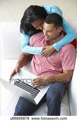 Stock Photo - Overhead View Of Couple Relaxing On Sofa Using Laptop. Fotosearch