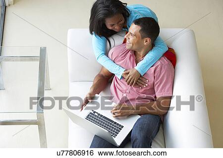 Stock Photograph - Overhead View Of Couple Relaxing On Sofa Using Laptop. Fotosearch