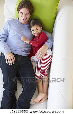 Stock Image - Overhead View Of Father And Daughter Relaxing On Sofa. Fotosearch