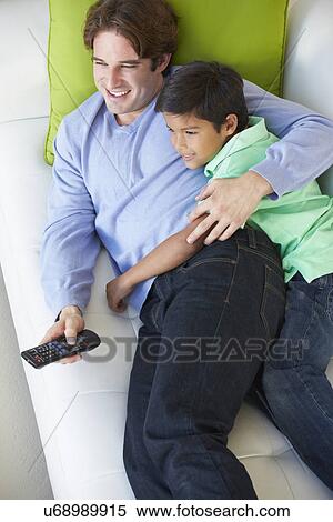 Stock Photography - Overhead View Of Father And Son Relaxing On Sofa Watching TV. Fotosearch