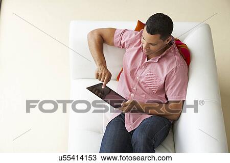 Stock Image - Overhead View Of Man Relaxing On Sofa Using Digital Tablet. Fotosearch