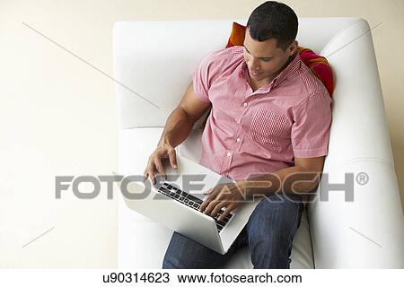 Stock Image - Overhead View Of Man Relaxing On Sofa Using Laptop. Fotosearch