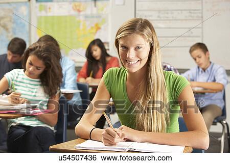 Stock Photograph - Portrait Of Female Pupil Studying At Desk In Classroom. Fotosearch