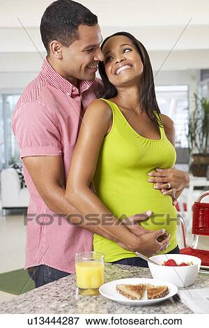 Stock Photo - Pregnant Woman And Husband Having Breakfast In Kitchen. Fotosearch