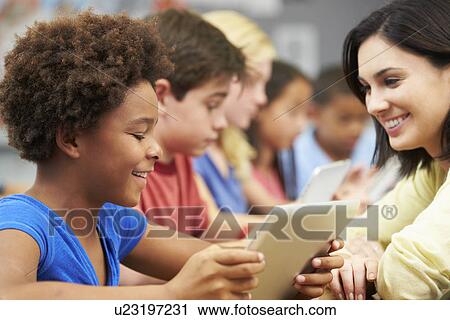 Stock Image - Pupils In Class Using Digital Tablet With Teacher. Fotosearch