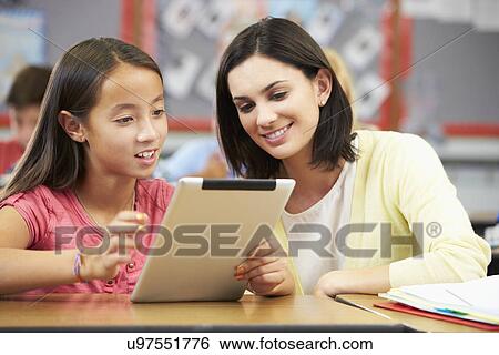 Stock Photograph - Pupils In Class Using Digital Tablet With Teacher. Fotosearch