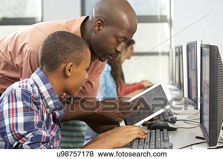 Teacher Helping Boy To Use Digital Tablet In Computer Class View Large Photo Image Stock Photo - Teacher Helping Boy To Use Digital Tablet In Computer Class. Fotosearch