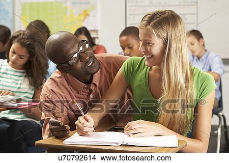 Teacher Helping Female Pupil Studying At Desk In Classroom View Large Photo Image Picture - Teacher Helping Female Pupil Studying At Desk In Classroom. Fotosearch