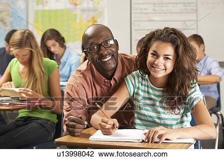 Teacher Helping Female Pupil Studying At Desk In Classroom View Large Photo Image Stock Image - Teacher Helping Female Pupil Studying At Desk In Classroom. Fotosearch