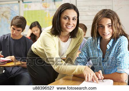 Teacher Helping Female Pupil Studying At Desk In Classroom View Large Photo Image Stock Photo - Teacher Helping Female Pupil Studying At Desk In Classroom. Fotosearch