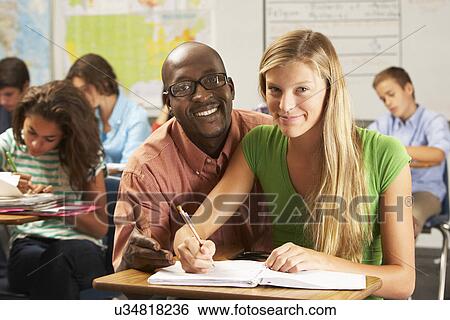 Teacher Helping Female Pupil Studying At Desk In Classroom View Large Photo Image Stock Photograph - Teacher Helping Female Pupil Studying At Desk In Classroom. Fotosearch