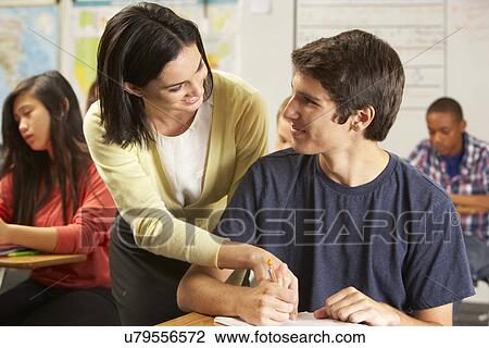 Teacher Helping Male Pupil Studying At Desk In Classroom View Large Photo Image Stock Image - Teacher Helping Male Pupil Studying At Desk In Classroom. Fotosearch