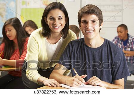 Teacher Helping Male Pupil Studying At Desk In Classroom View Large Photo Image Stock Image - Teacher Helping Male Pupil Studying At Desk In Classroom. Fotosearch