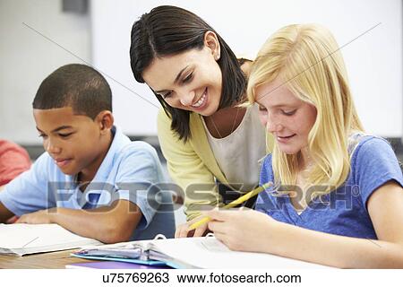 Teacher Helping Pupils Studying At Desks In Classroom View Large Photo Image Stock Image - Teacher Helping Pupils Studying At Desks In Classroom. Fotosearch