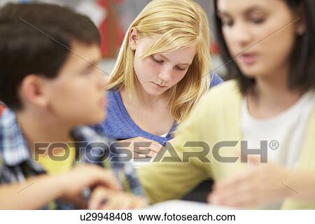 Stock Photo - Teacher Helping Pupils Studying At Desks In Classroom. Fotosearch